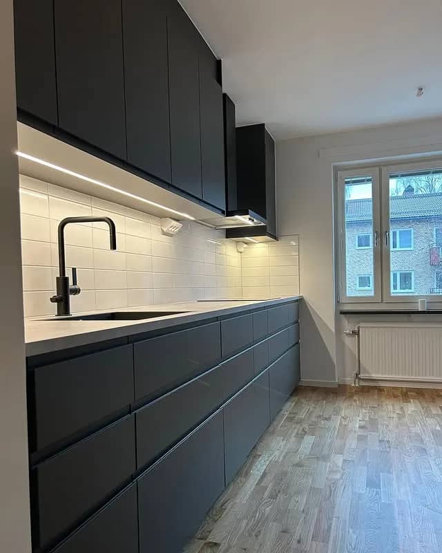 Kök med svarta skåp, vitt kakel, grå bänkskiva och trägolv